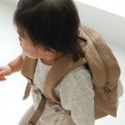 Child wearing a beige backpack on a white background