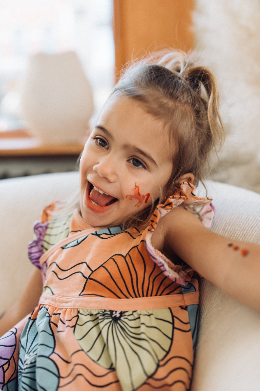 Young girl with butterfly-themed dress and face paint sitting on a couch.