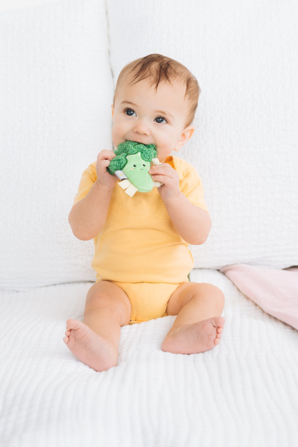 Baby sitting on a white bed holding a green toy