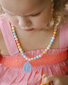 Child wearing a colorful beaded necklace with a pink dress
