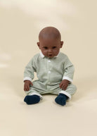 Baby wearing a striped onesie sitting on a beige background