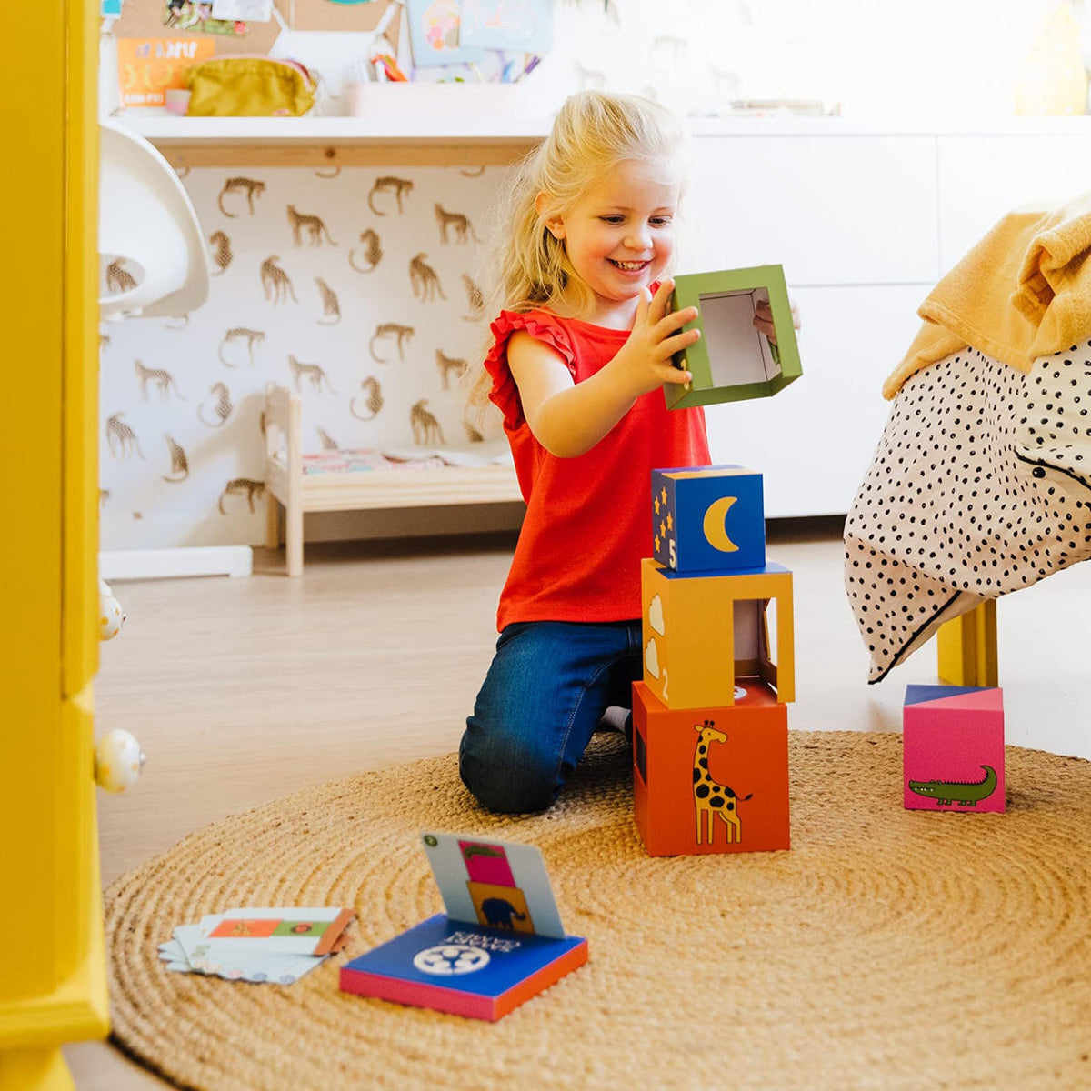 Child playing with colorful blocks on a rug in a room with animal-patterned wallpaper.