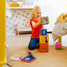 Child playing with colorful blocks on a rug in a room with animal-patterned wallpaper.