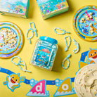 Baby Shark-themed party supplies including plates, cups, and candy on a yellow background