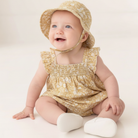 Baby wearing a yellow floral outfit and hat on a white background
