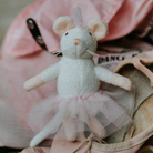 Stuffed mouse toy with a tutu dress on a pink surface