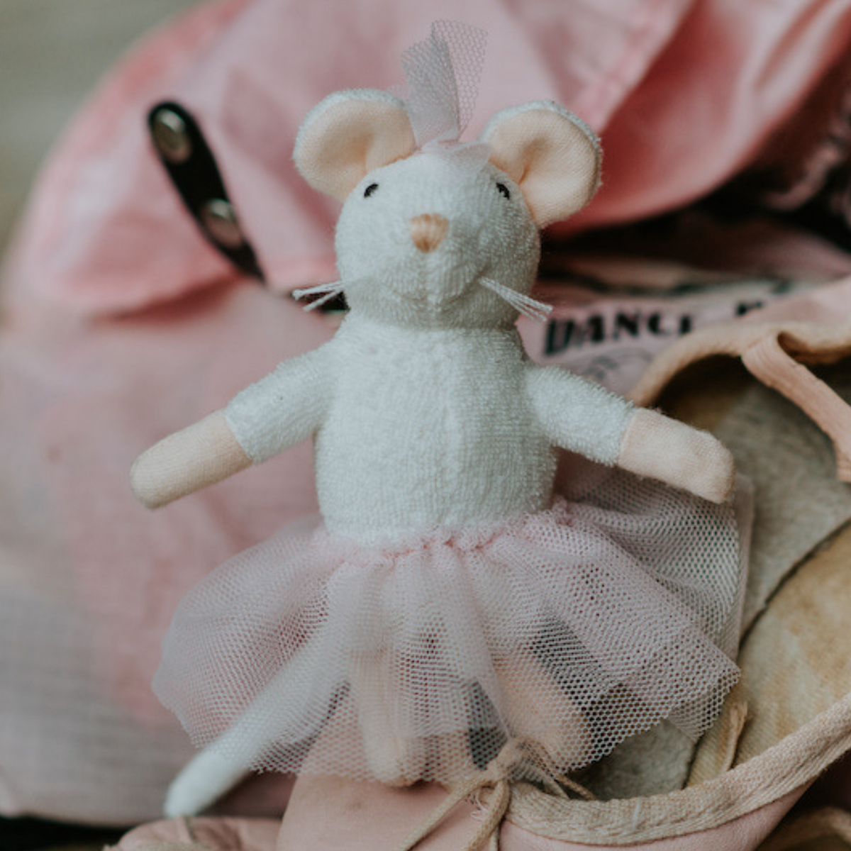Stuffed mouse toy with a tutu dress on a pink surface
