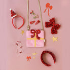 Decorative items including a pink gift box, red sequin headbands, and gold stars on a pink background