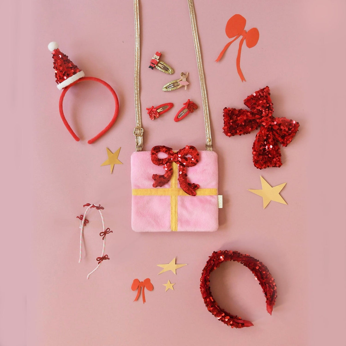 Decorative items including a pink gift box, red sequin headbands, and gold stars on a pink background