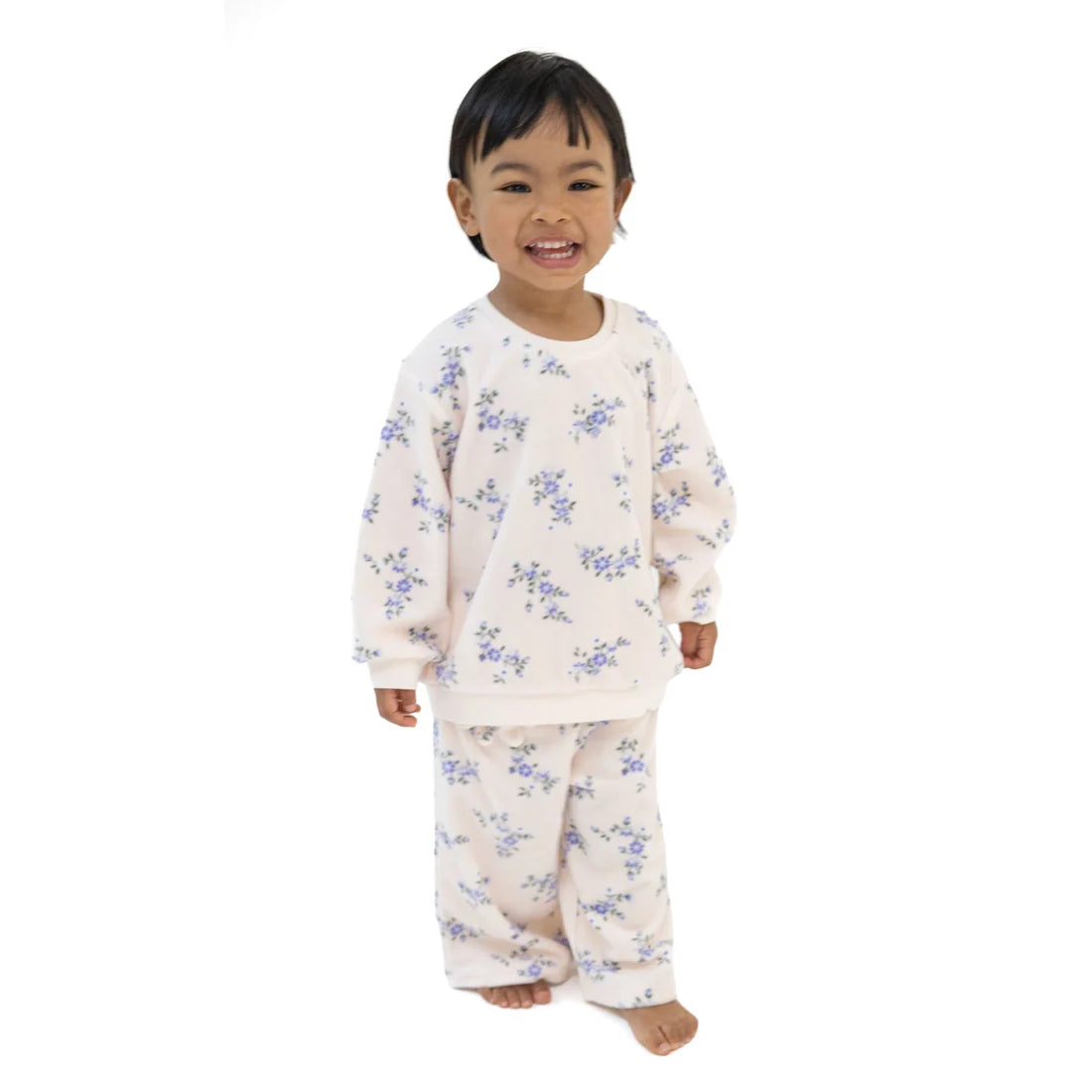 A smiling young child wearing a two-piece pajama set with a light cream base and a blue floral pattern, standing against a plain white background.