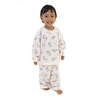 A smiling young child wearing a two-piece pajama set with a light cream base and a blue floral pattern, standing against a plain white background.