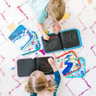 Two children playing with colorful drawing boards on a patterned rug.