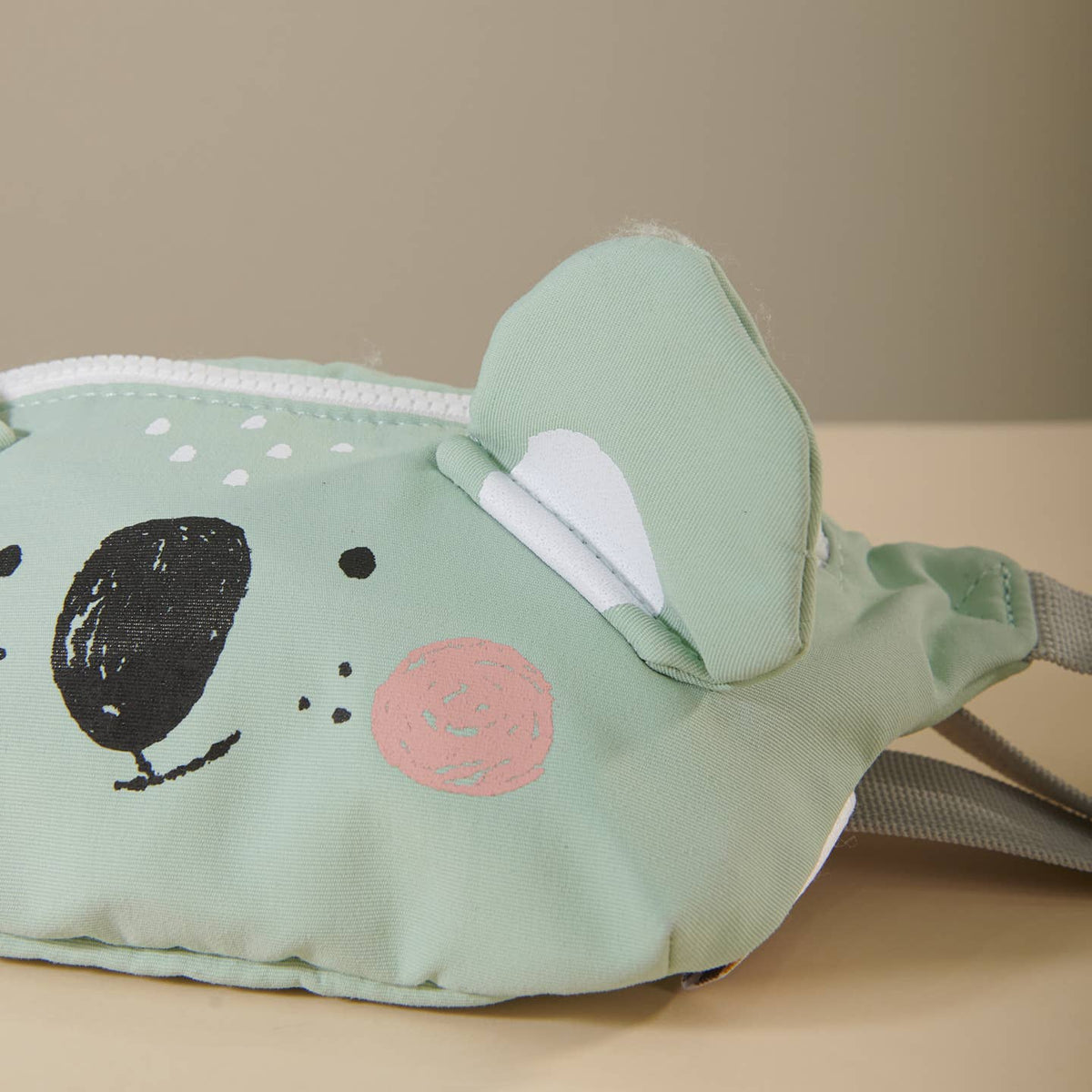 Green animal-shaped pouch with a face on a beige surface