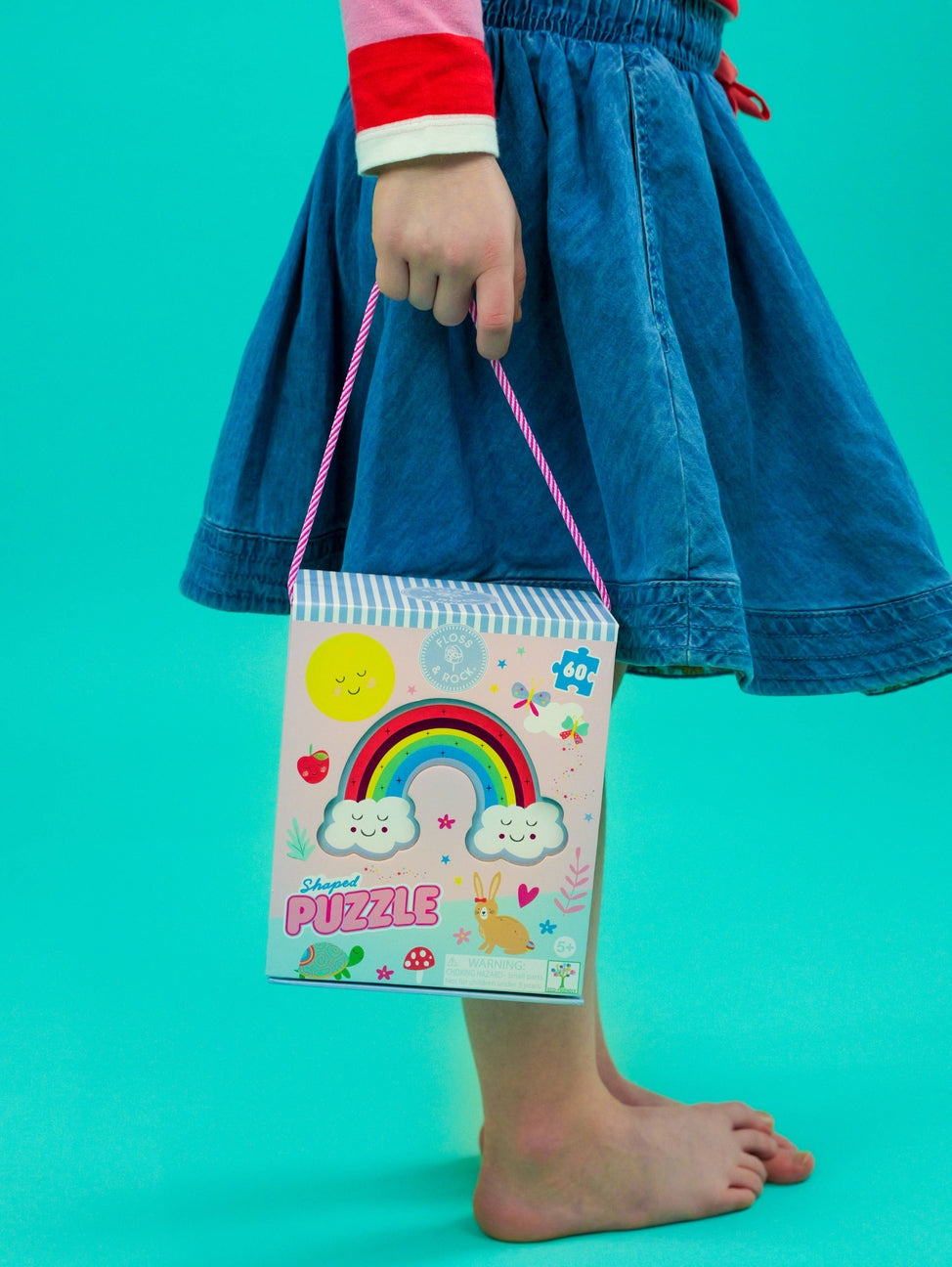 Child holding a colorful puzzle box with a rainbow design against a teal background