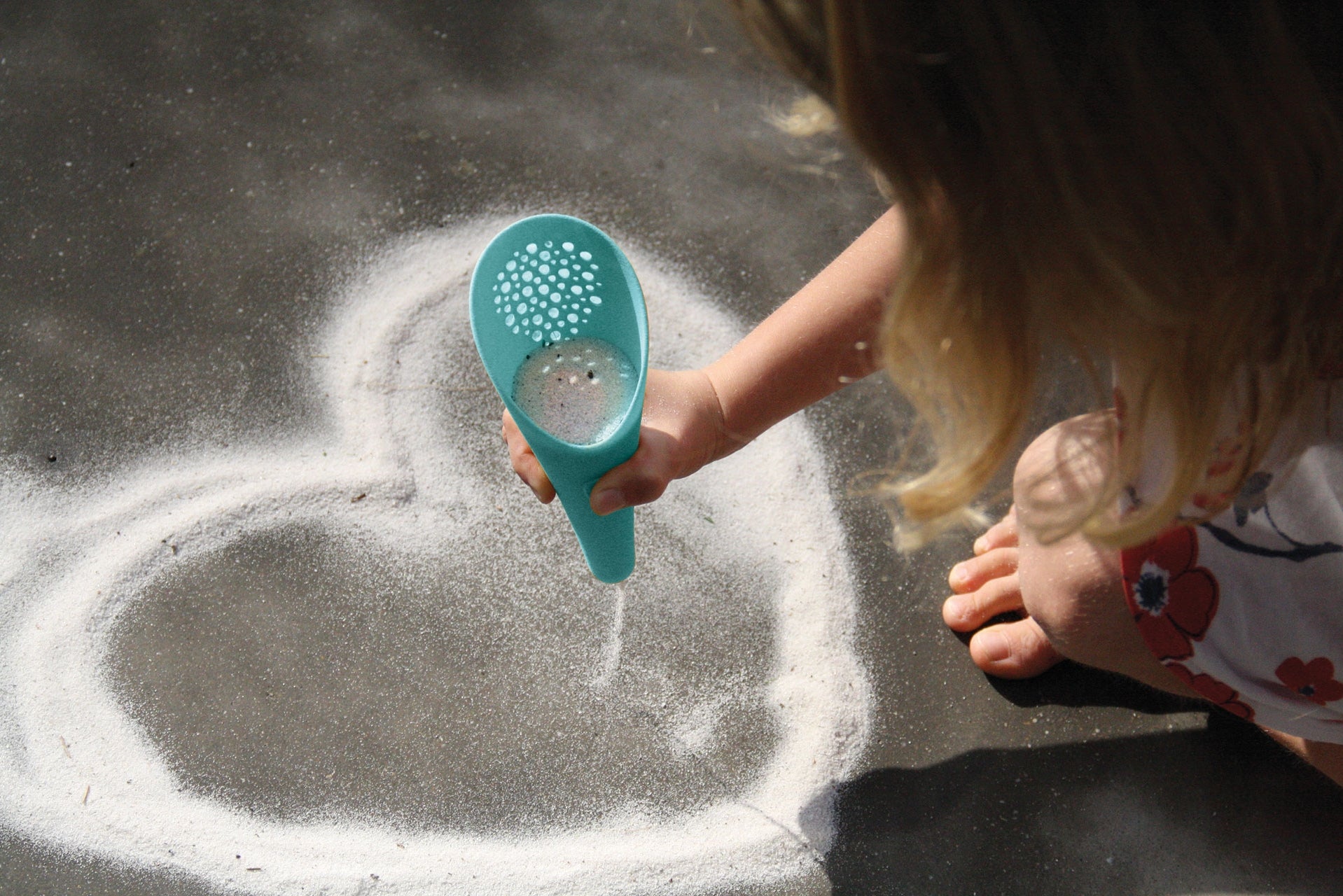Child playing with a blue sand toy on a sandy surface
