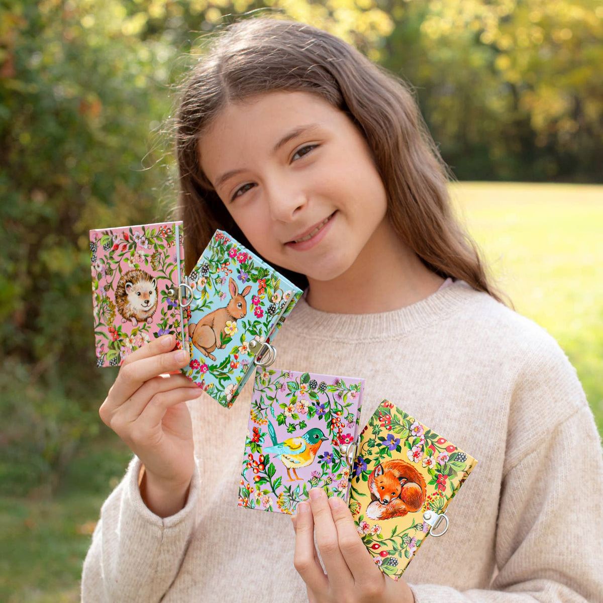 Girl holding four colorful animal-themed notebooks outdoors