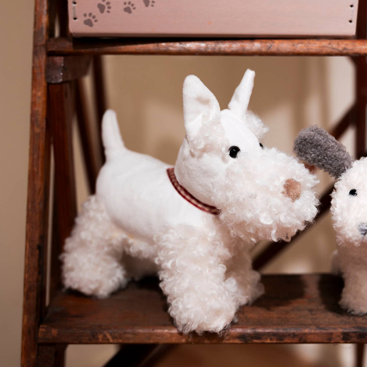 Two white plush dogs on a wooden shelf with a blurred background