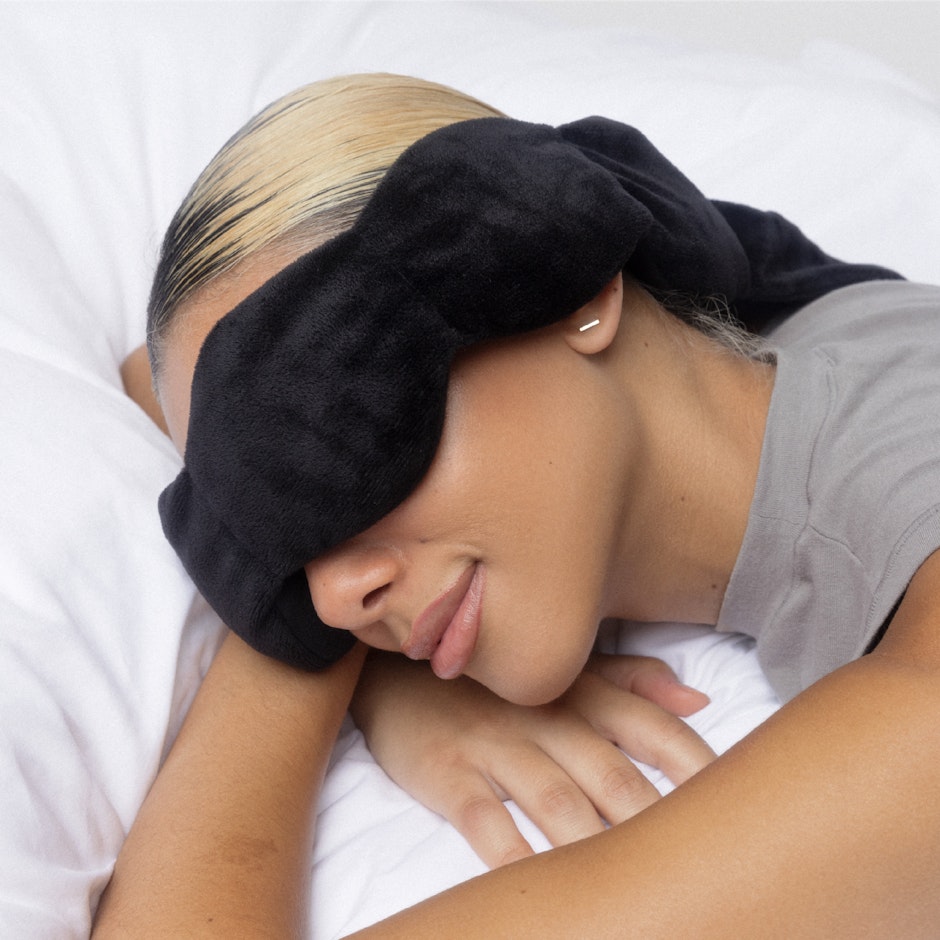 Person wearing a black sleep mask on a white background