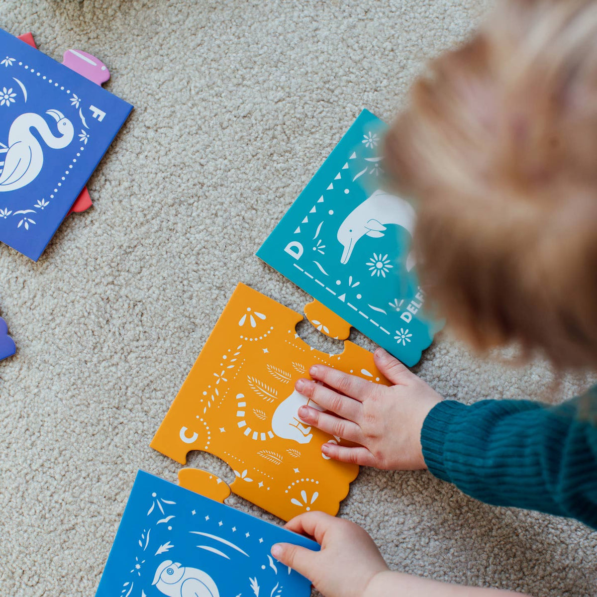 Child playing with colorful animal-themed puzzle pieces on a carpeted floor.
