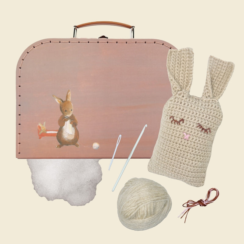 Pink suitcase with a rabbit design, crochet bunny, yarn, and knitting needles on a beige background