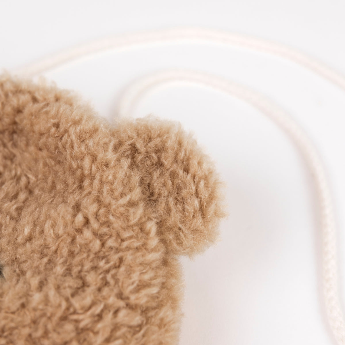 Close-up of a beige curly faux-fur texture with a thin cream cord or strap on a plain white background.