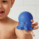 Child holding a blue octopus-shaped toy with water features, against a bathroom background.