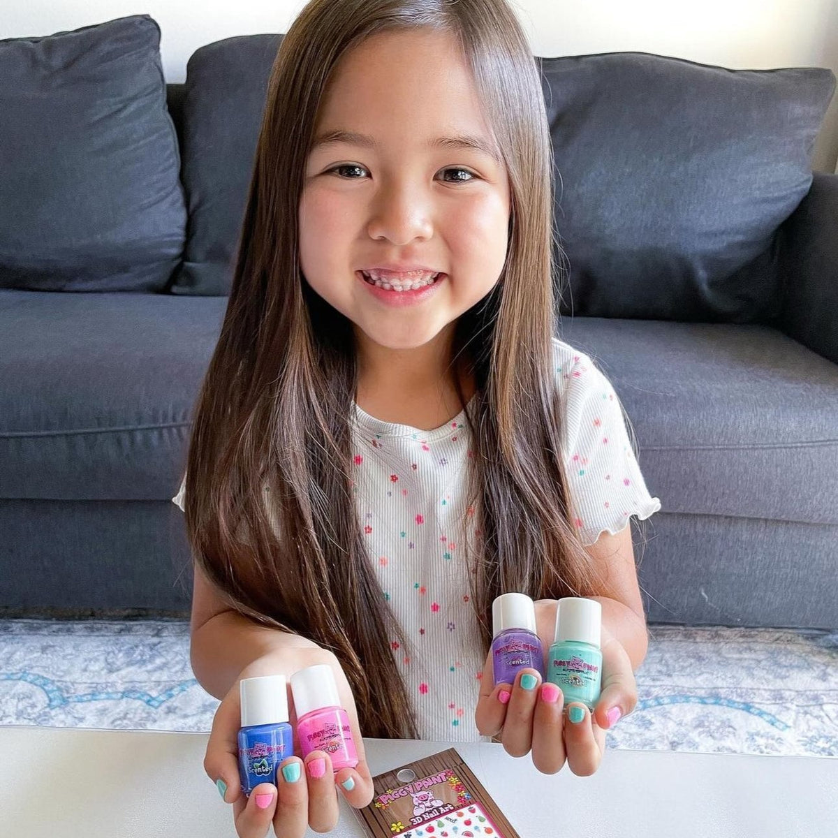 Young girl holding colorful nail polish bottles in a living room setting