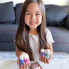 Young girl holding colorful nail polish bottles in a living room setting