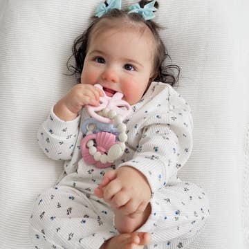 Baby lying on a white blanket with a toy in its mouth