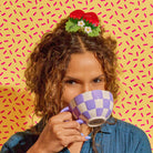 Woman drinking from a checkered mug with a colorful background