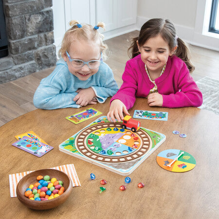Two children playing with a board game on a wooden floor.