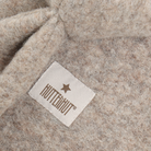 A close-up detail of the camel melange wool blend fabric showing the stitched Huttelihut brand label with a star.