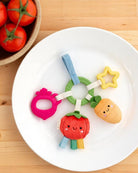 Colorful baby teething toy on a white plate with tomatoes in the background