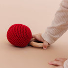 Red knitted ball and wooden ring on a beige surface with a child's hand reaching towards them.