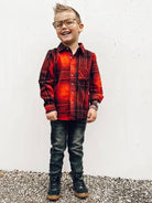 Child wearing a red plaid shirt and jeans standing on a textured surface with a white background