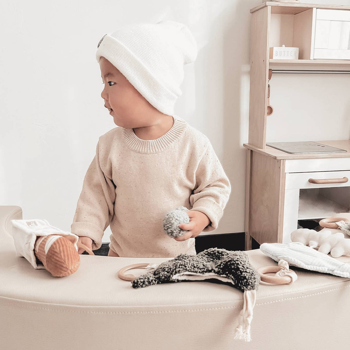 Child playing with toys on a light-colored surface in a minimalistic room.