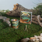 Candle and matches with nature-themed packaging on a mossy surface