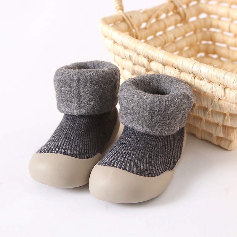Pair of gray baby shoes with beige soles next to a woven basket on a white background