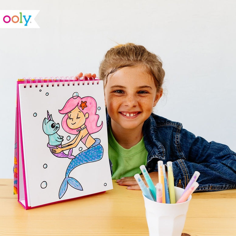 Child holding a coloring book with a mermaid drawing, surrounded by colorful markers.