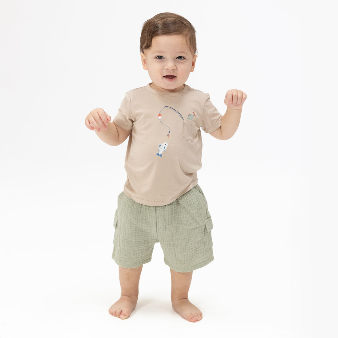 Child wearing a beige shirt with cartoon characters and green shorts on a white background