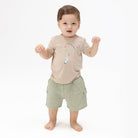 Child wearing a beige shirt with cartoon characters and green shorts on a white background