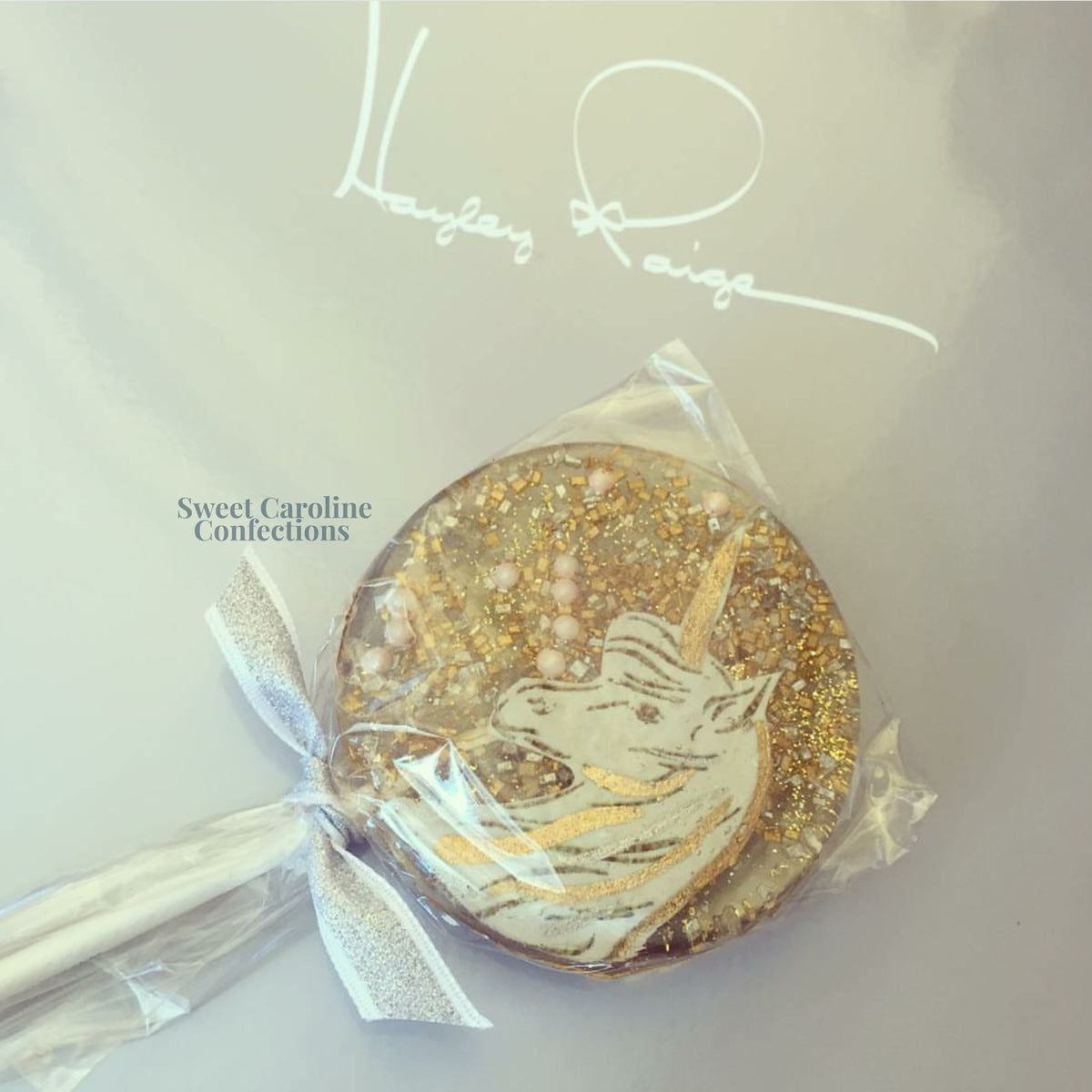 Decorative lollipop with gold and white design, branded 'Sweet Caroline Confections'.