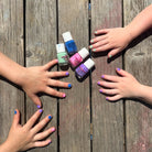 Five hands with colorful nail polish reaching towards five small bottles of nail polish on a wooden surface.