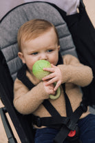 An infant sitting in a stroller chews on a green cabbage-shaped teether toy.