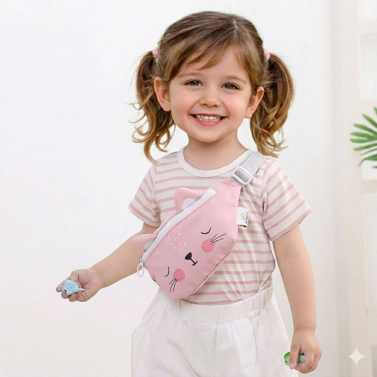 Child wearing a pink cat-shaped fanny pack against a white background