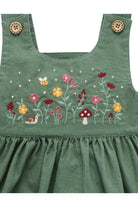 Green corduroy baby dress featuring colorful embroidered wildflowers, a mushroom, a bee, and a snail on the chest, with decorative wooden buttons on the shoulder straps.