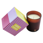 A lavender-berry scented candle in an amber glass jar next to its geometric, multicolored packaging box on a white background.