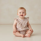 Baby wearing a floral romper sitting on a plain background