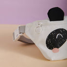 White fanny pack with black and pink design on a beige surface with purple background