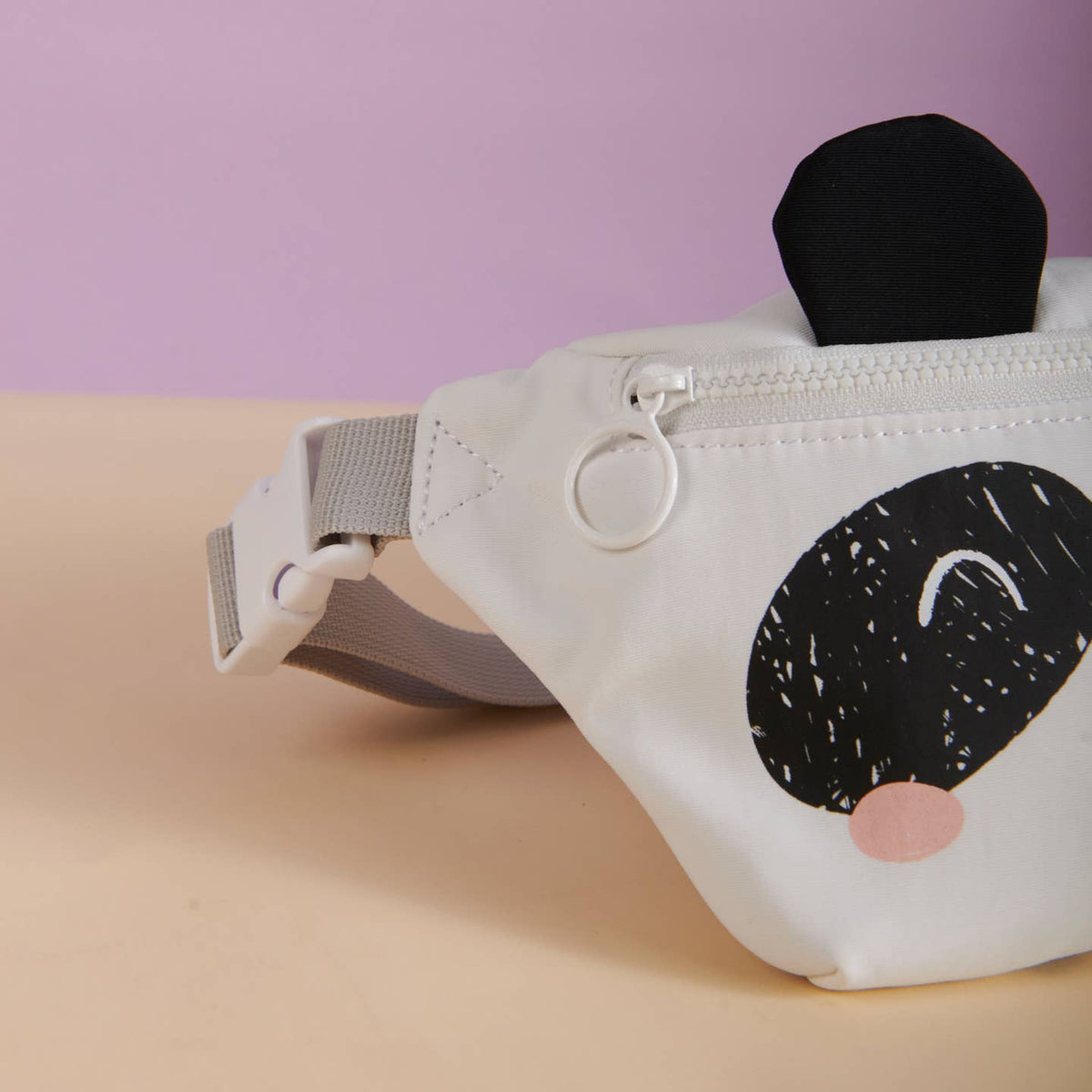 White fanny pack with black and pink design on a beige surface with purple background